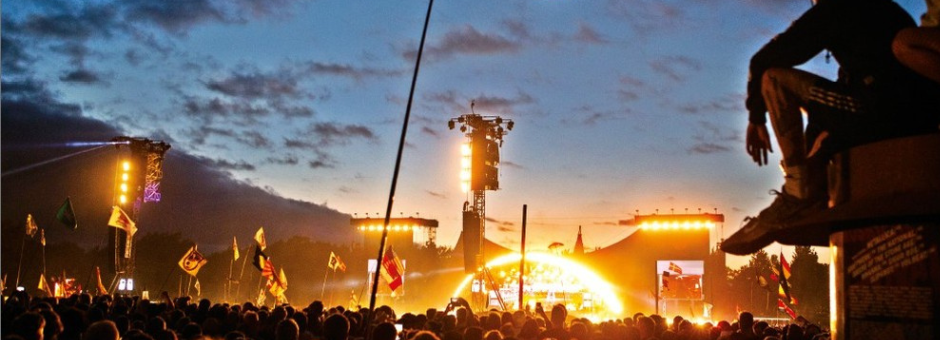 Roskilde Festival Mainstage bei Dunkelheit. Vorne eine Person die auf einer Erhöhung sitzt